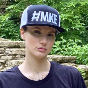 Woman wearing a black and white flat brim hat with big and bold white lettering of # M K E.